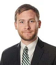 Man in a suit and tie smiles at the camera against a white backdrop.