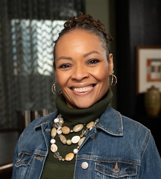 Woman with a warm smile wearing a denim jacket and green turtleneck indoors.