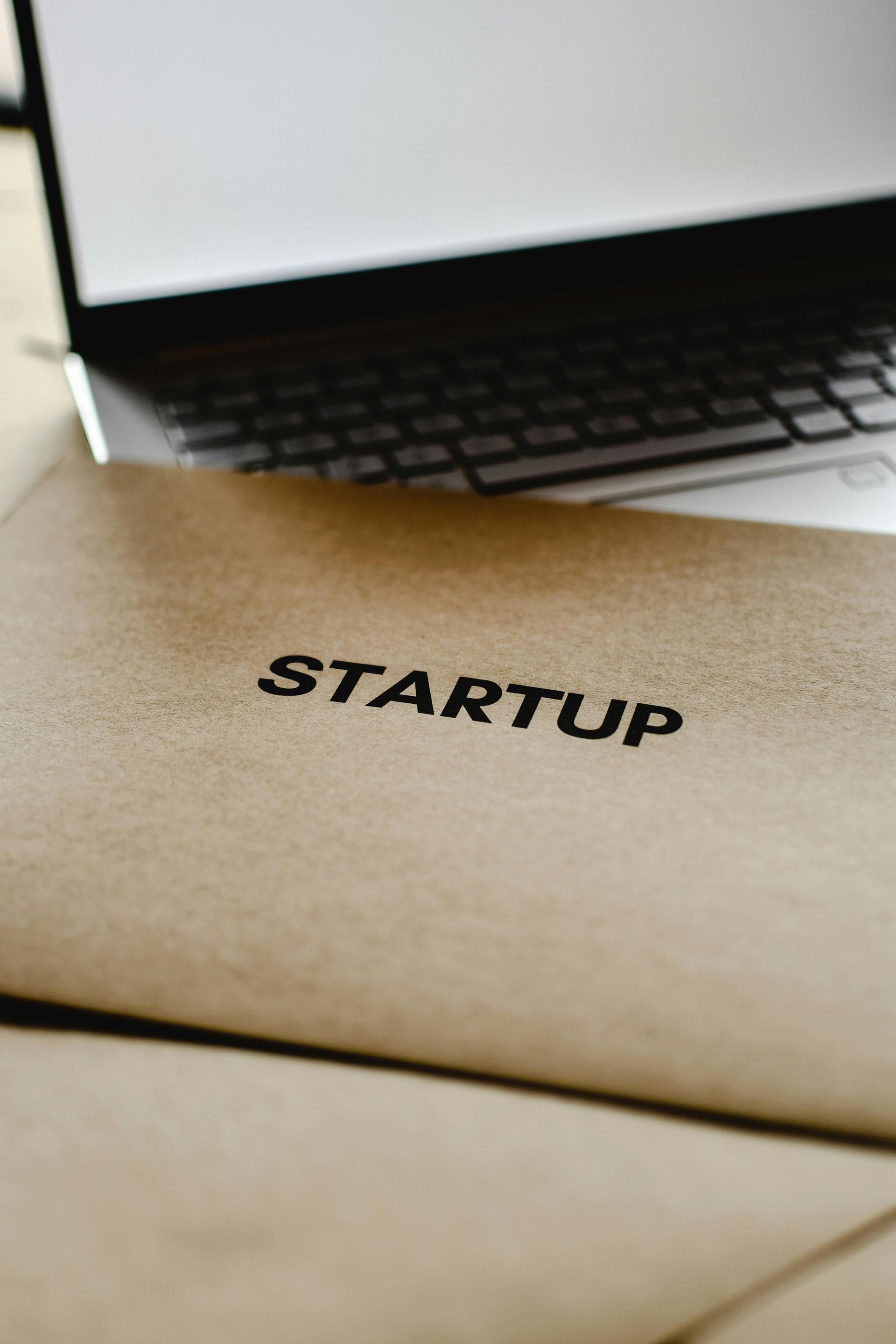 Brown envelope stamped STARTUP in front of a laptop on a desk.