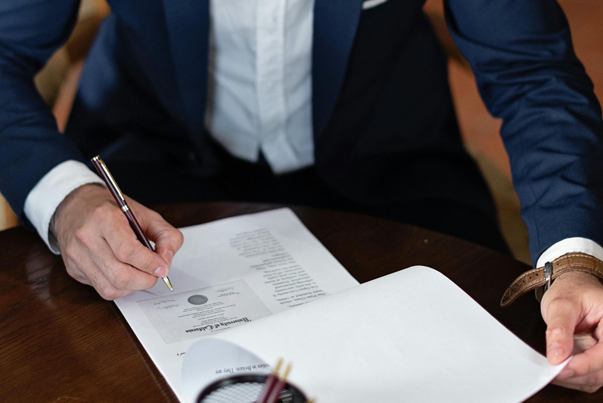 Person in a blue suit signing a document at a desk with papers and a pen