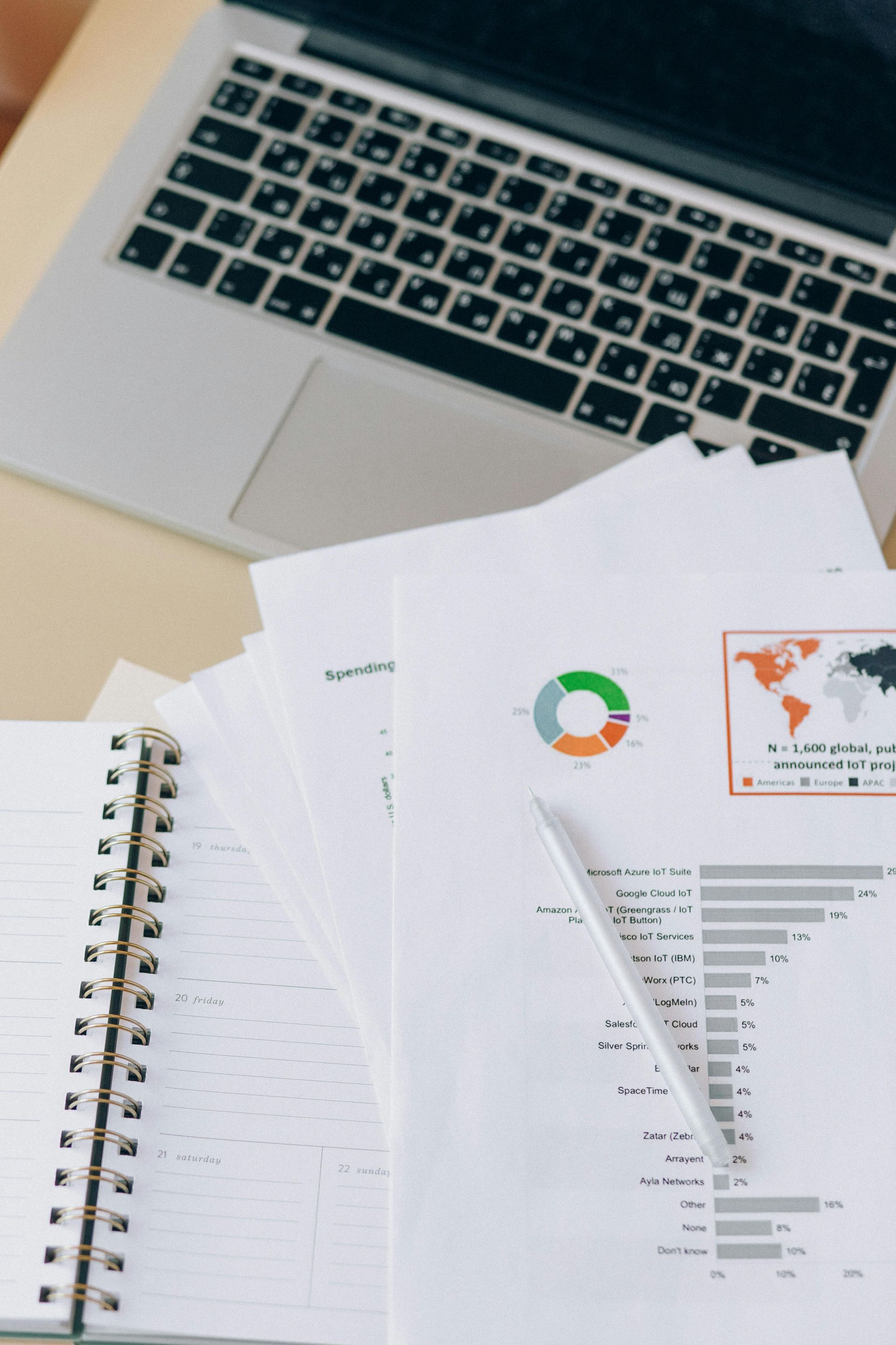 A laptop is sitting on a desk next to a notebook and papers