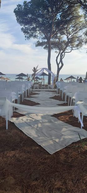 Cerimonia nuziale sulla spiaggia; sedie bianche, navata, arco, oceano sullo sfondo.