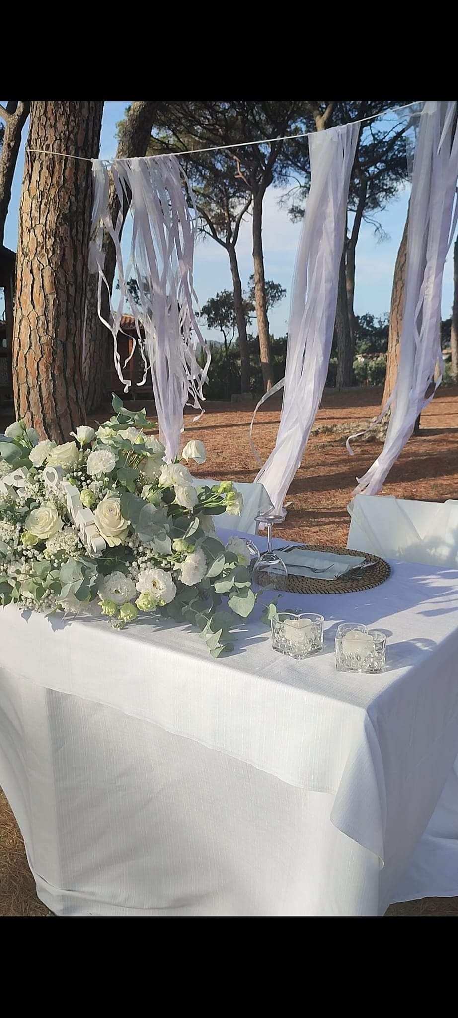 Composizione floreale bianca su un tavolo con drappeggio bianco; allestimento per matrimonio all'aperto.