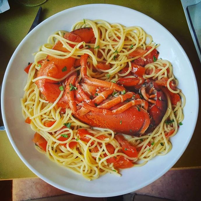 Spaghetti con aragosta, salsa rossa ed erbe aromatiche in una ciotola bianca.