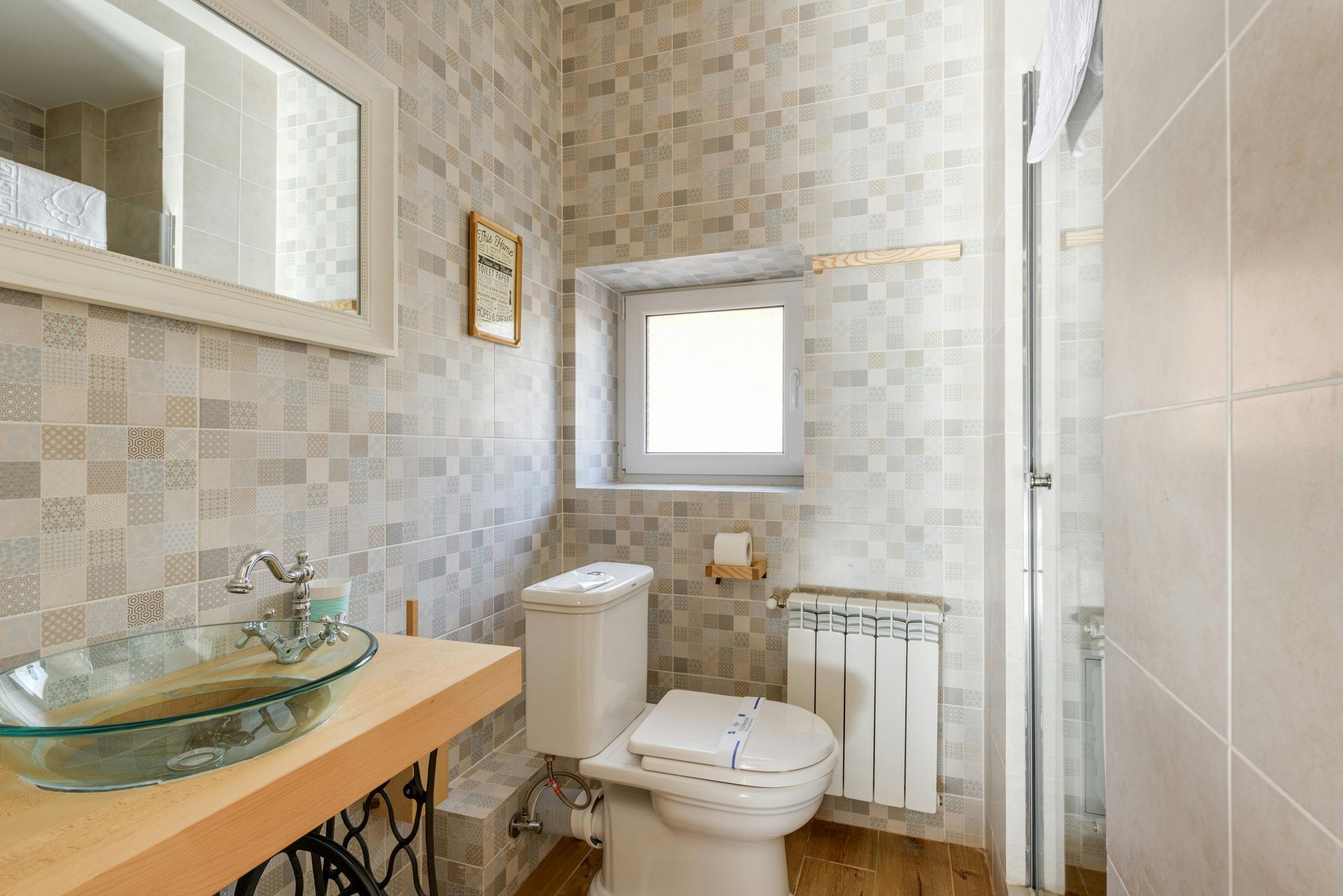 Bathroom with a glass sink, toilet, small window, and light-colored tiled walls and floors.