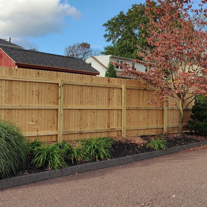 A wooden fence in front of a house with a tree in the background
