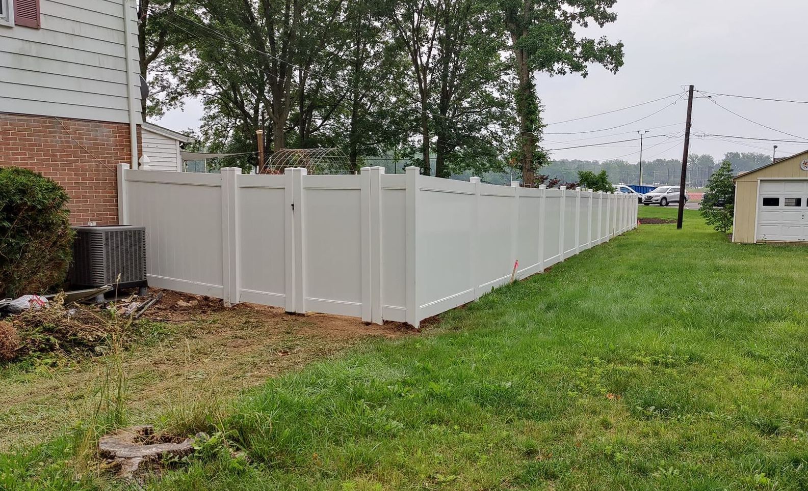 A white fence surrounds a lush green yard in front of a house.