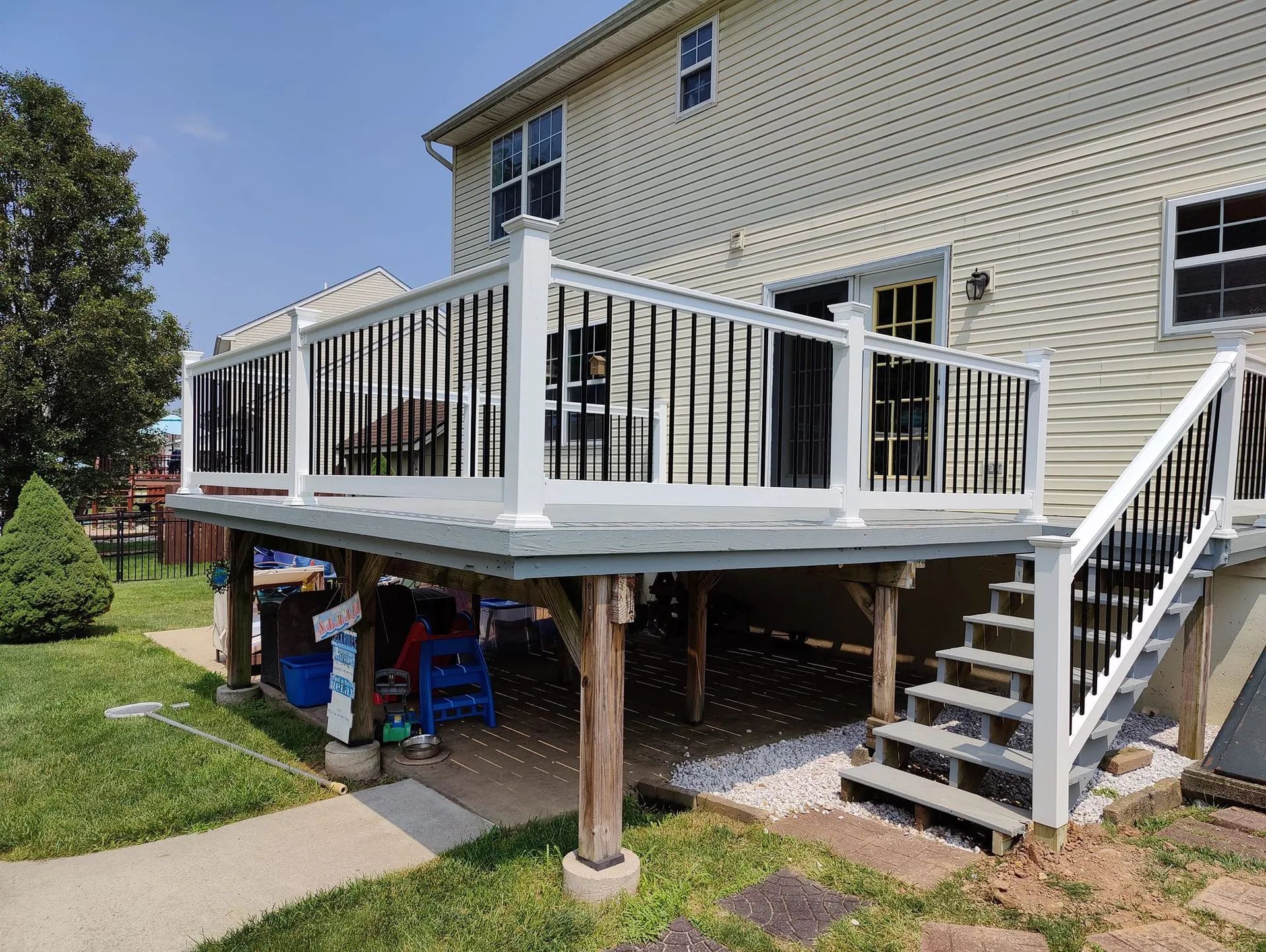 Elevated wooden deck attached to a light-colored house with white railing and stairs. Below is a patio.
