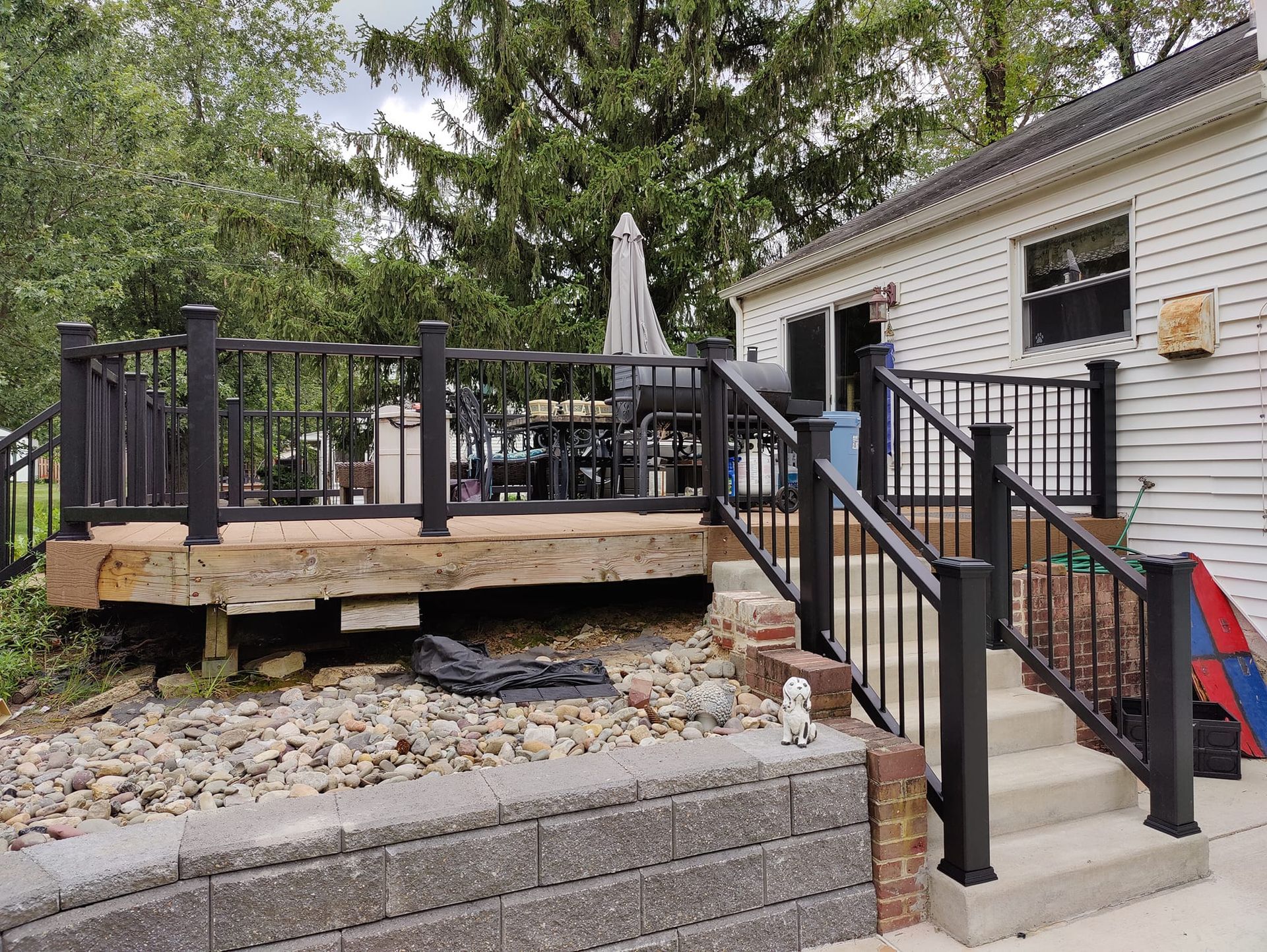 A deck with stairs leading up to it and a white house in the background.