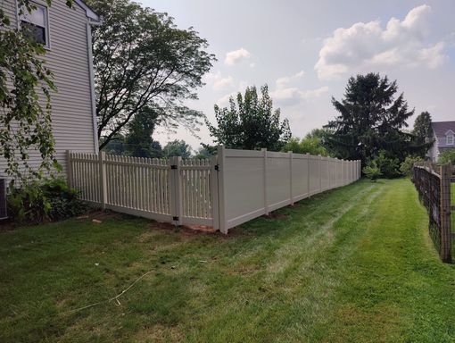 A white fence surrounds a lush green yard next to a house.