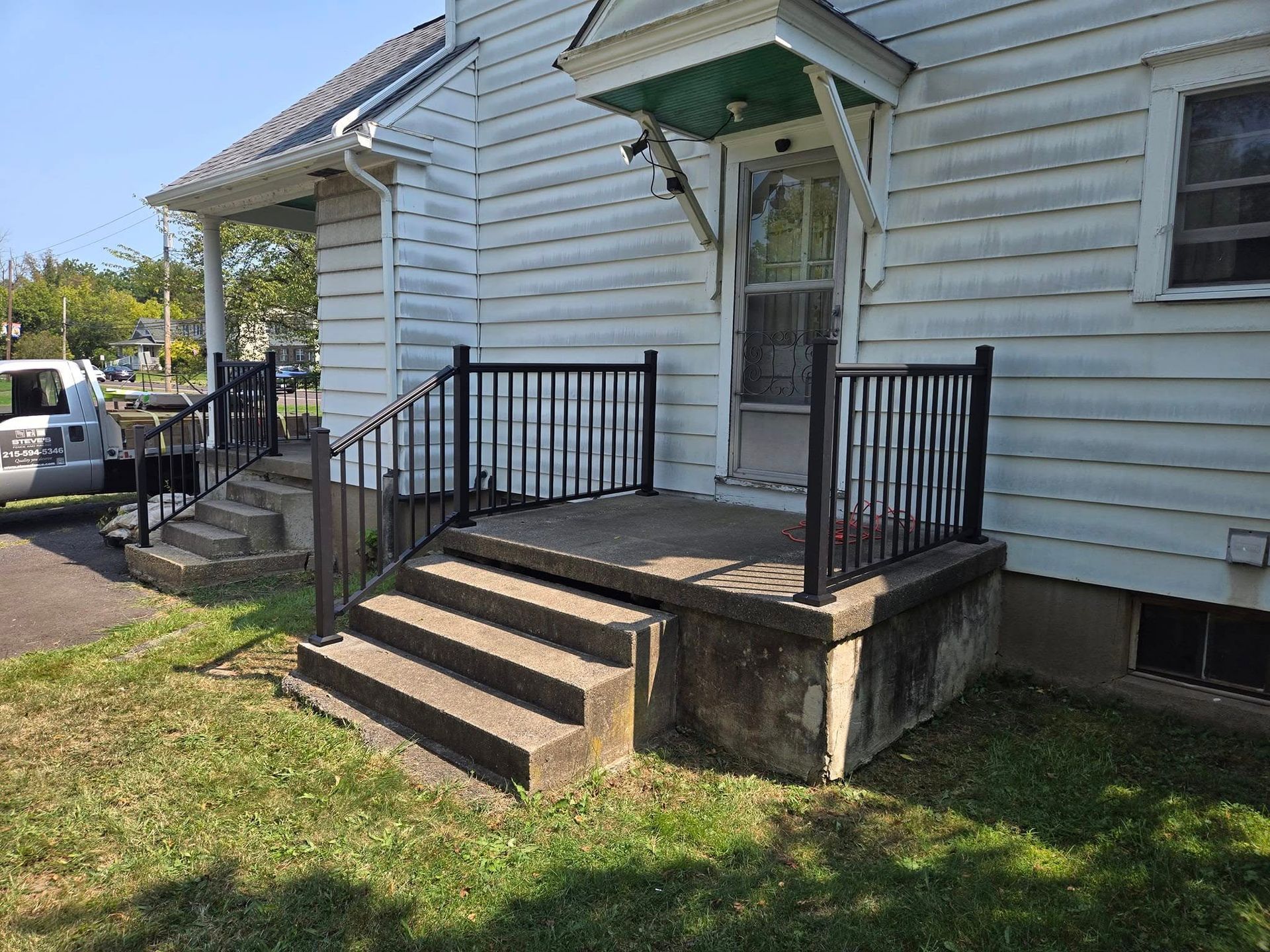 A white house with a porch and stairs and a car parked in front of it.