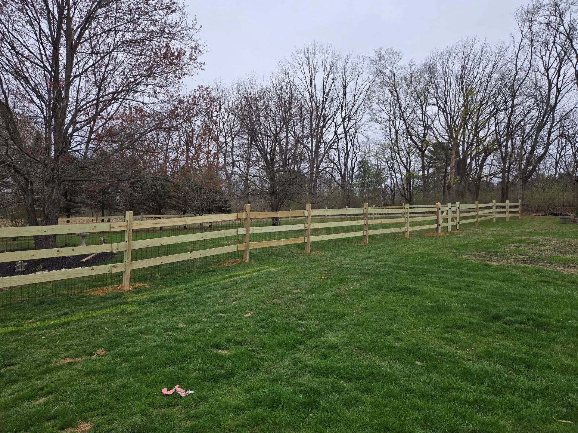 A wooden fence surrounds a grassy field with trees in the background.