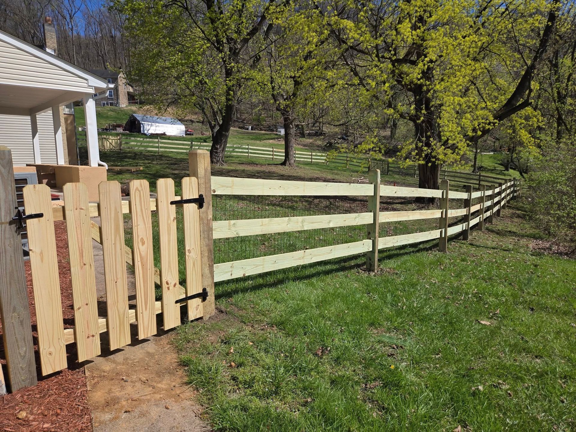 A wooden fence surrounds a grassy field next to a house.