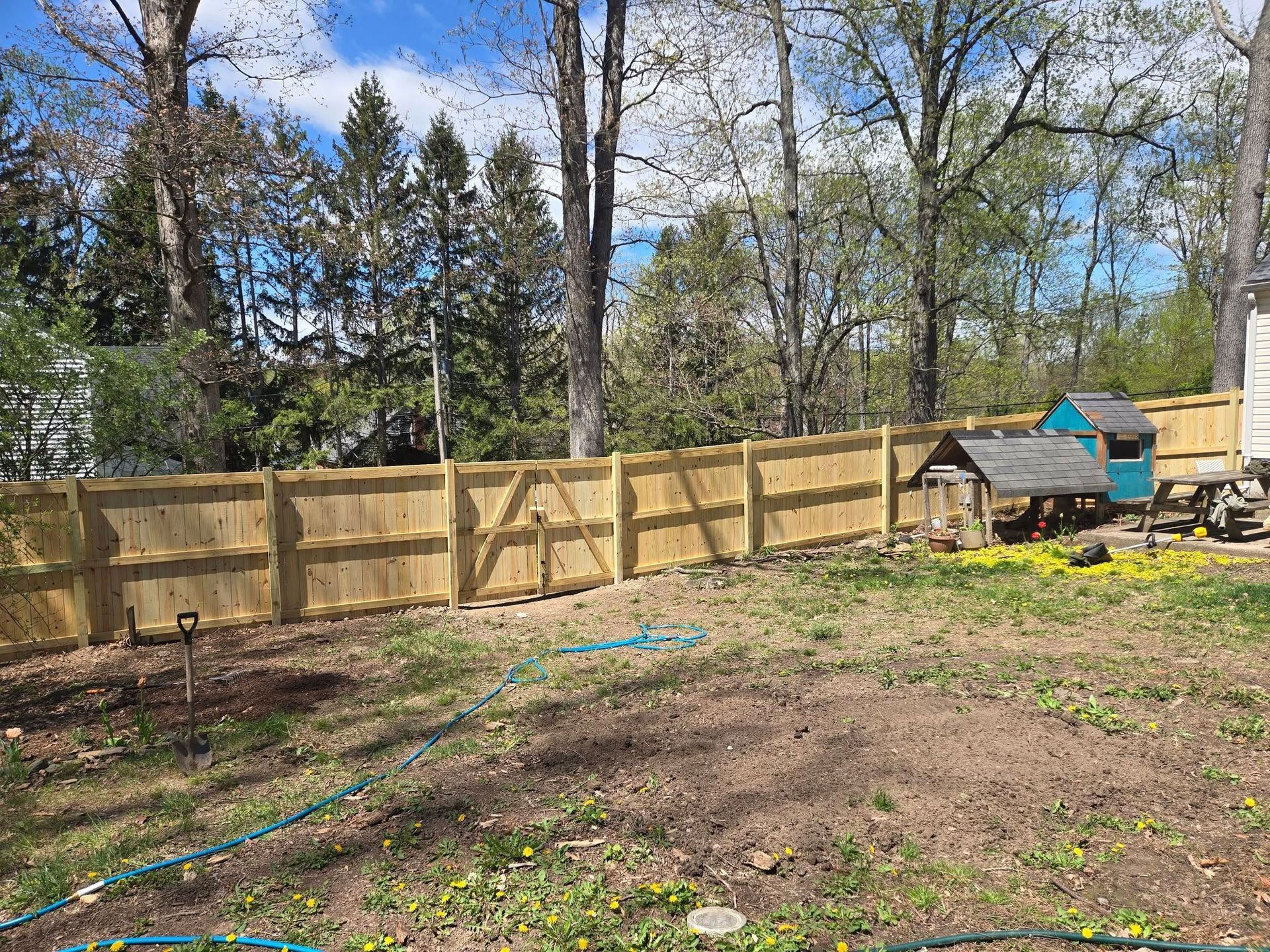 A wooden fence in a backyard with a chicken coop in the background.