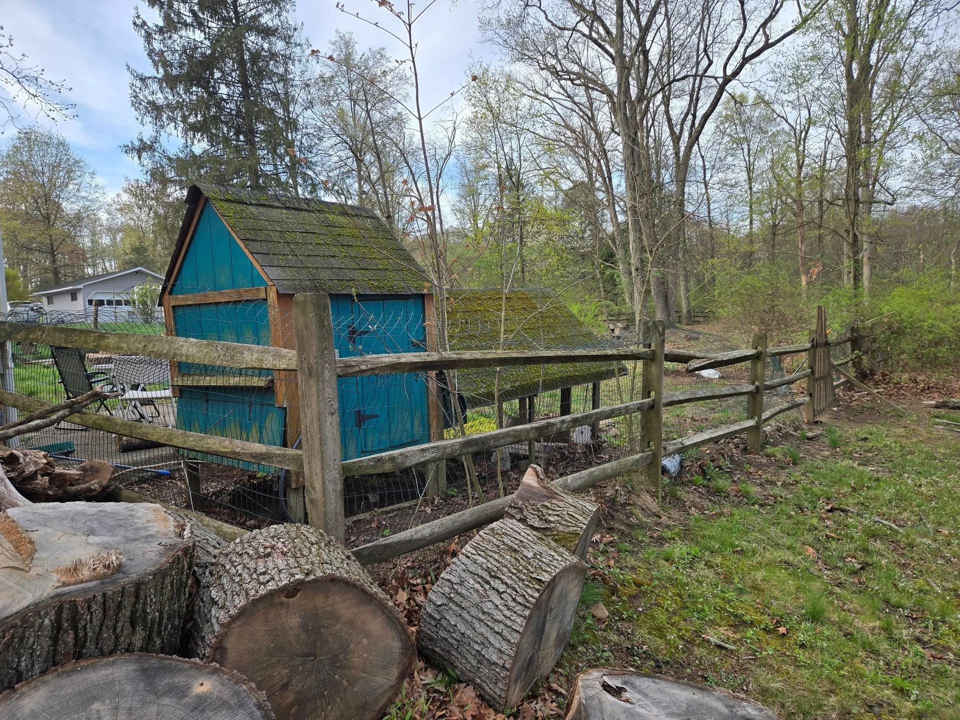 A blue shed is sitting next to a wooden fence in a field.