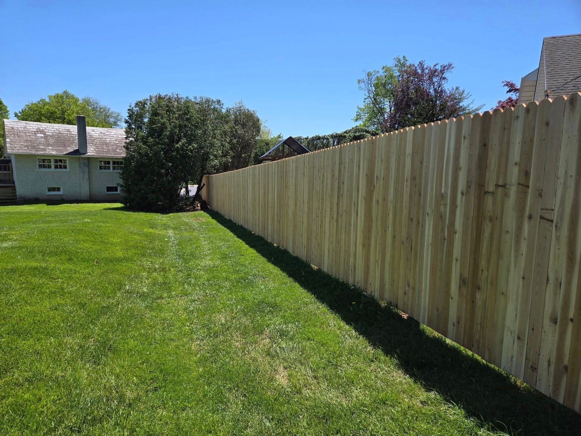 A wooden fence surrounds a lush green yard in front of a house.