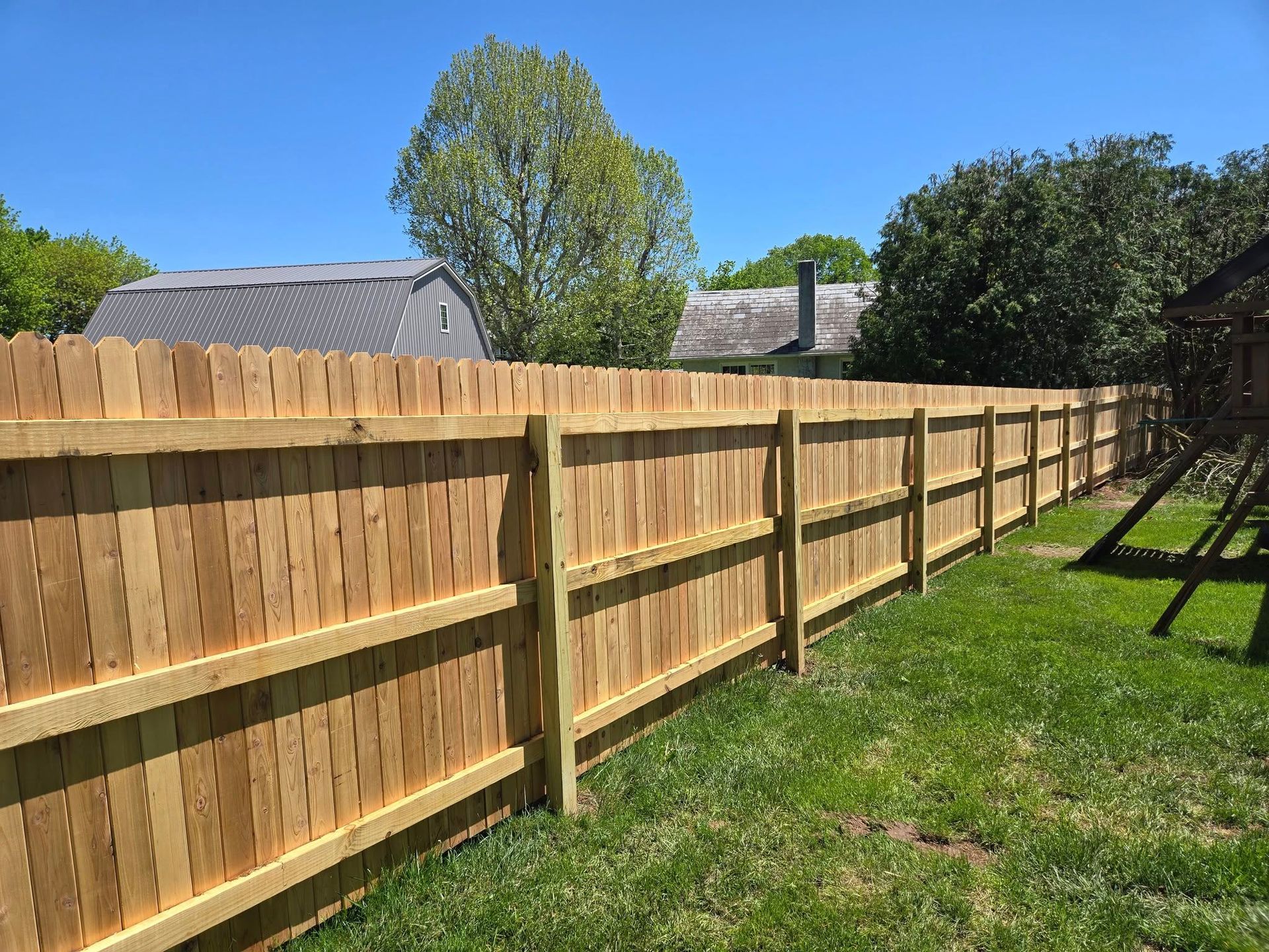 A wooden fence in a backyard with a house in the background.