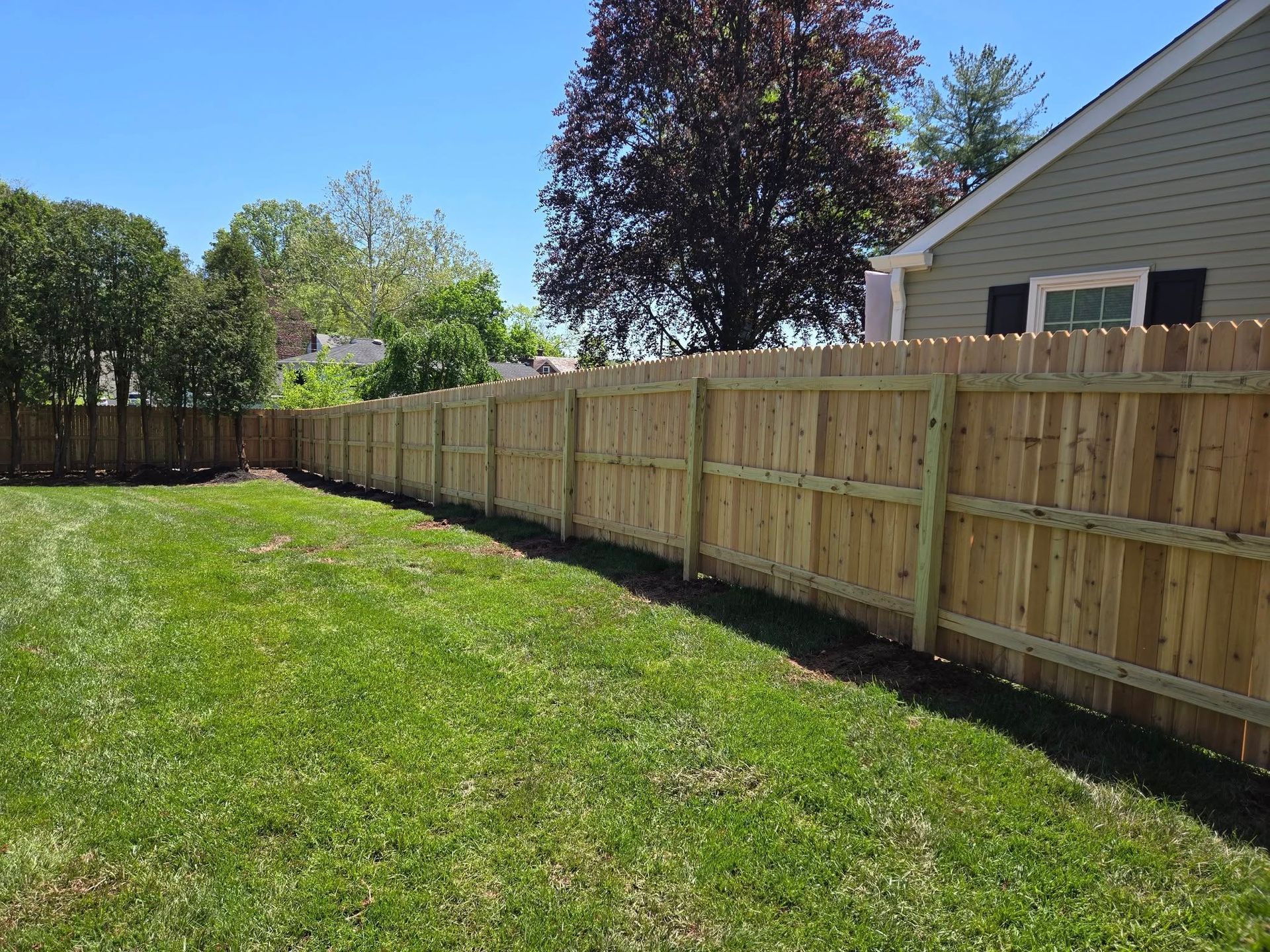 A wooden fence surrounds a lush green yard in front of a house.