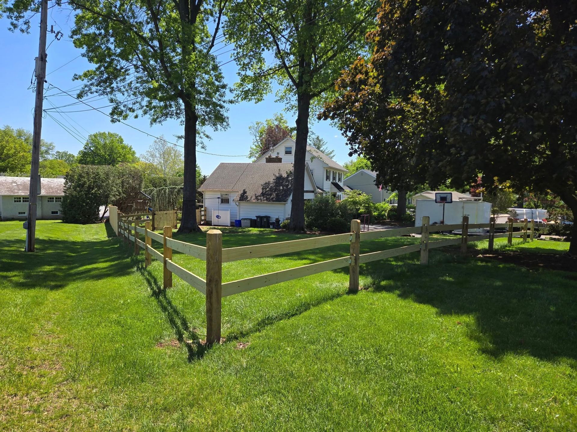 A wooden fence surrounds a lush green field in front of a house.