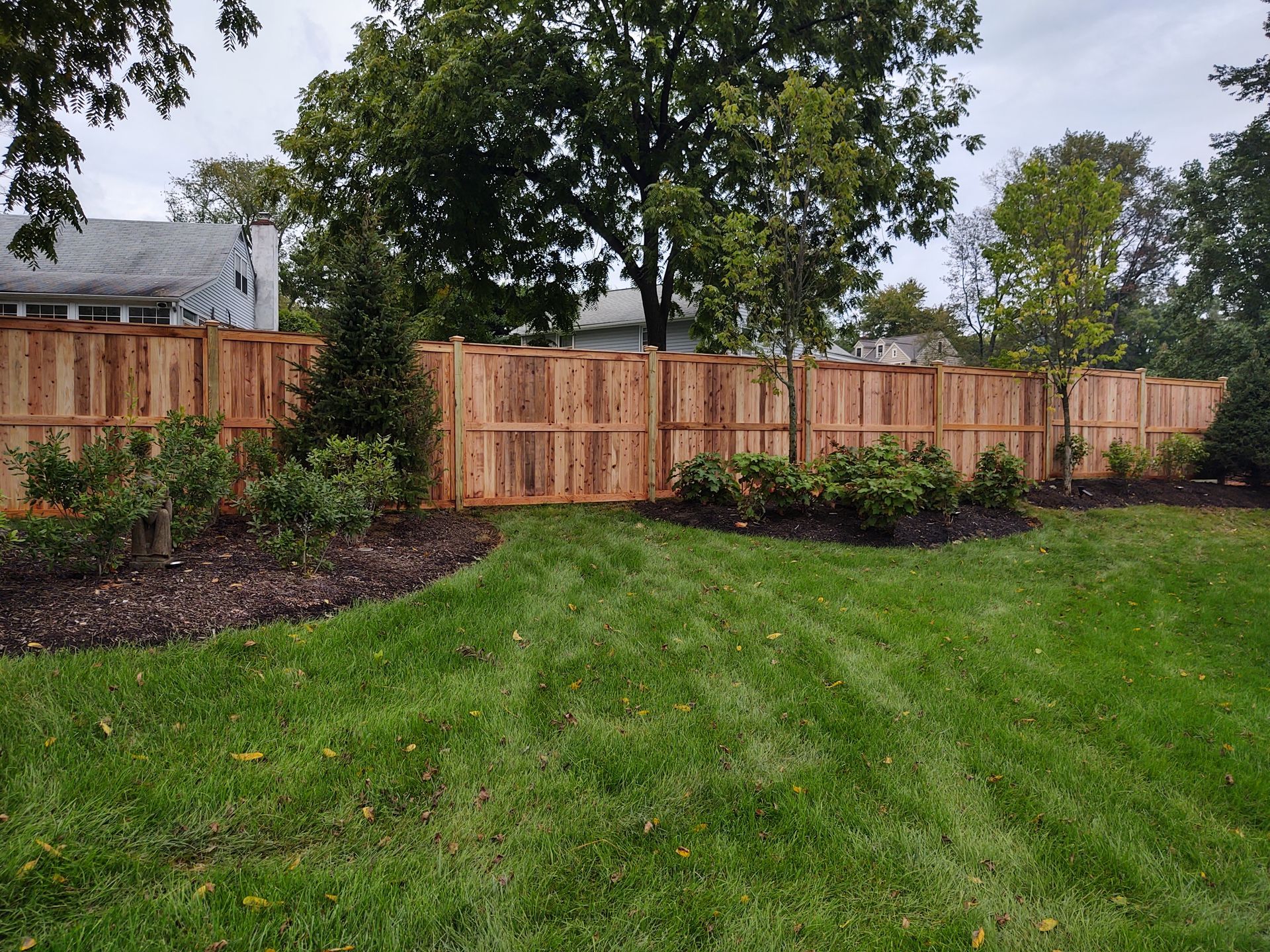 A wooden fence surrounds a lush green lawn in a backyard.