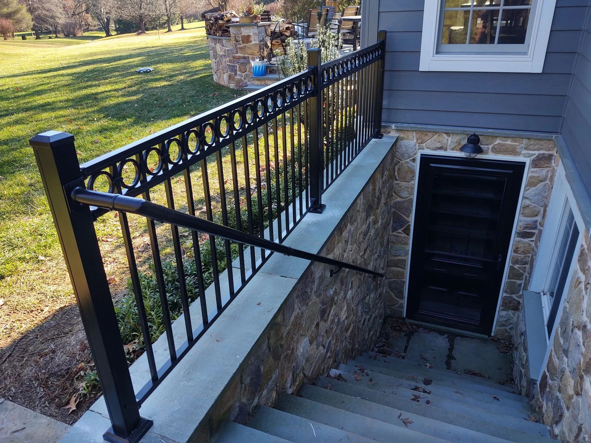 Black railing with decorative circles along stone steps leading to a basement door.