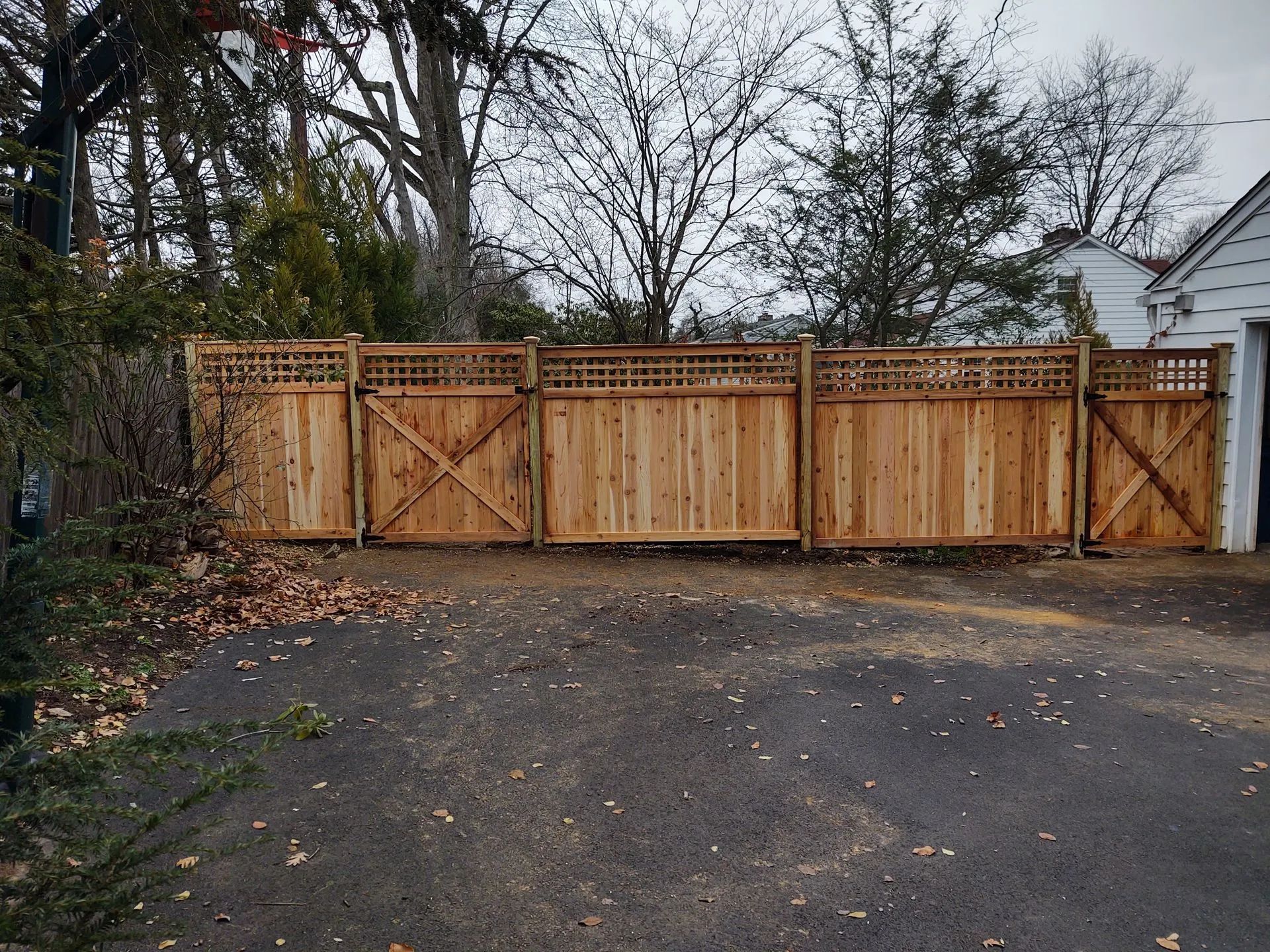 Wooden fence with lattice top, gates, and trees against a cloudy sky.