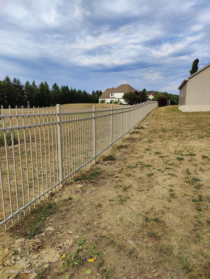 A metal fence surrounds a grassy field with a house in the background.