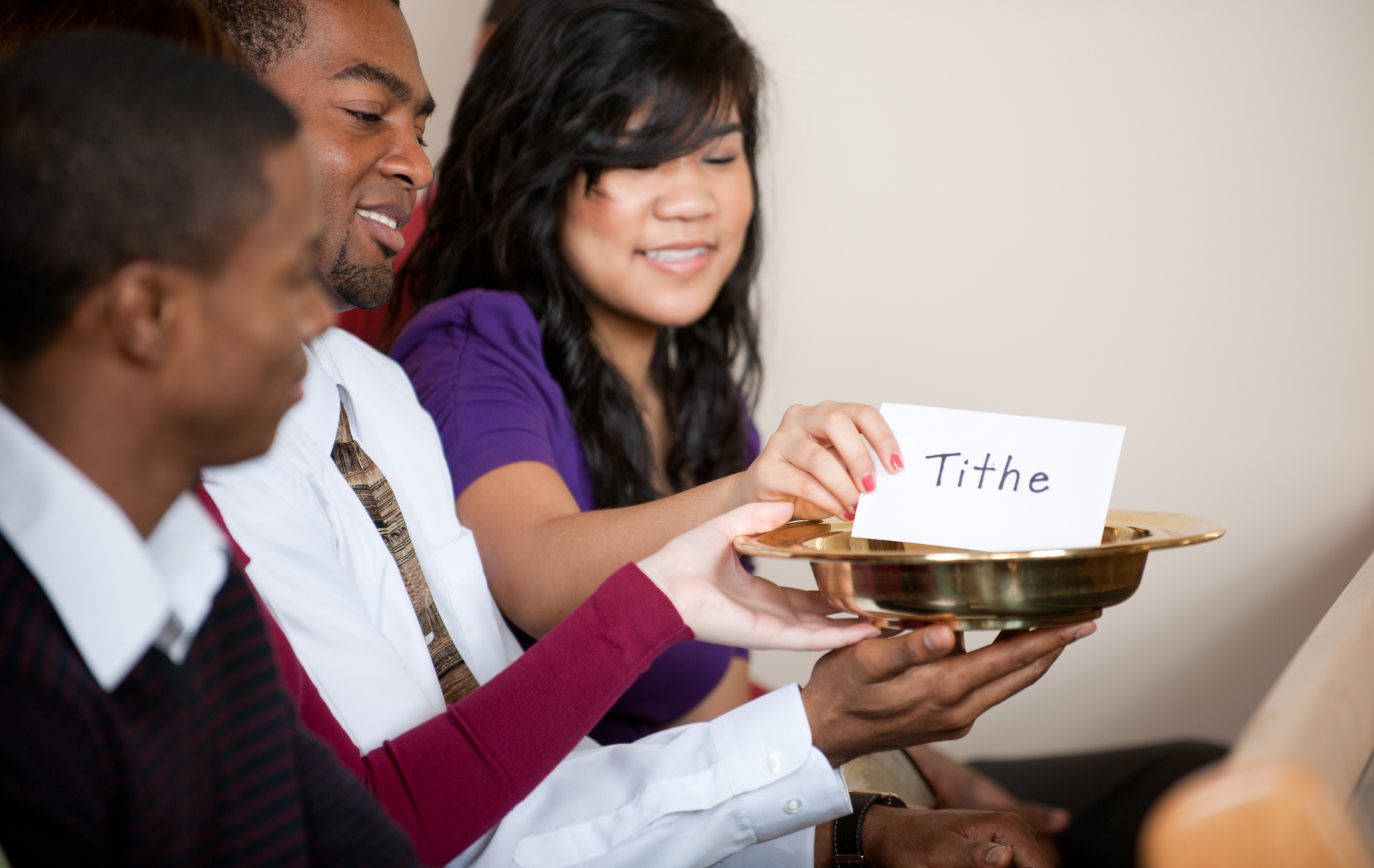 a group of people are sitting around a tray with a card that says tithe on it .