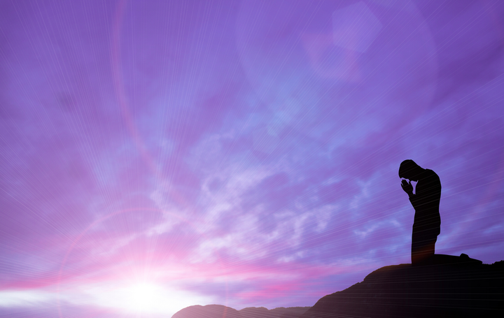 a silhouette of a man praying on top of a hill at sunset .