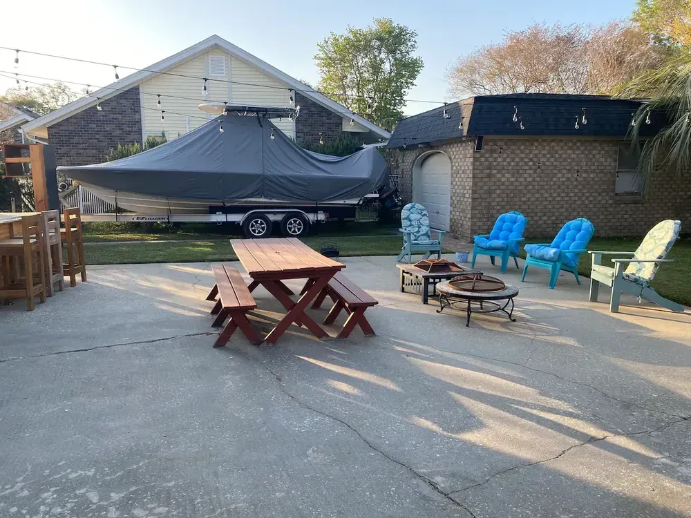A boat is sitting on a trailer in a driveway next to a picnic table and chairs.