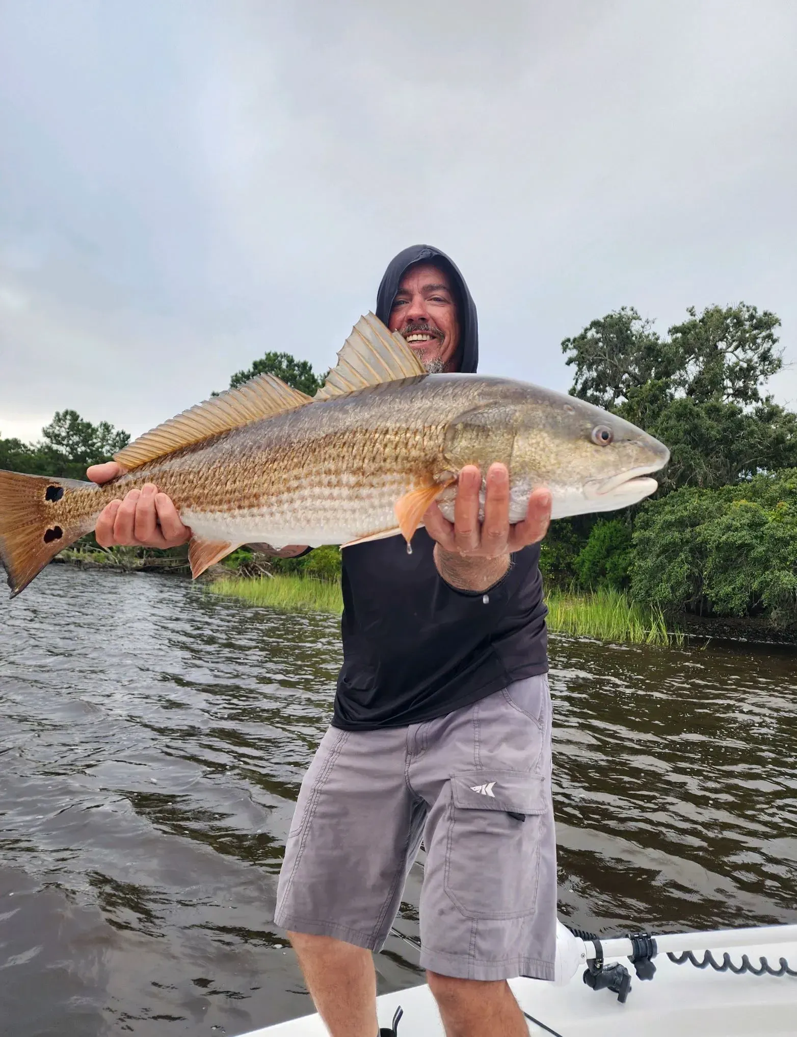 A man is holding a large fish in his hands while standing on a boat.