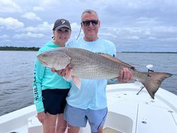 A man and a woman are standing on a boat holding a large fish.
