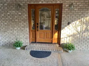 The front door of a brick house with a wooden door and a black mat.