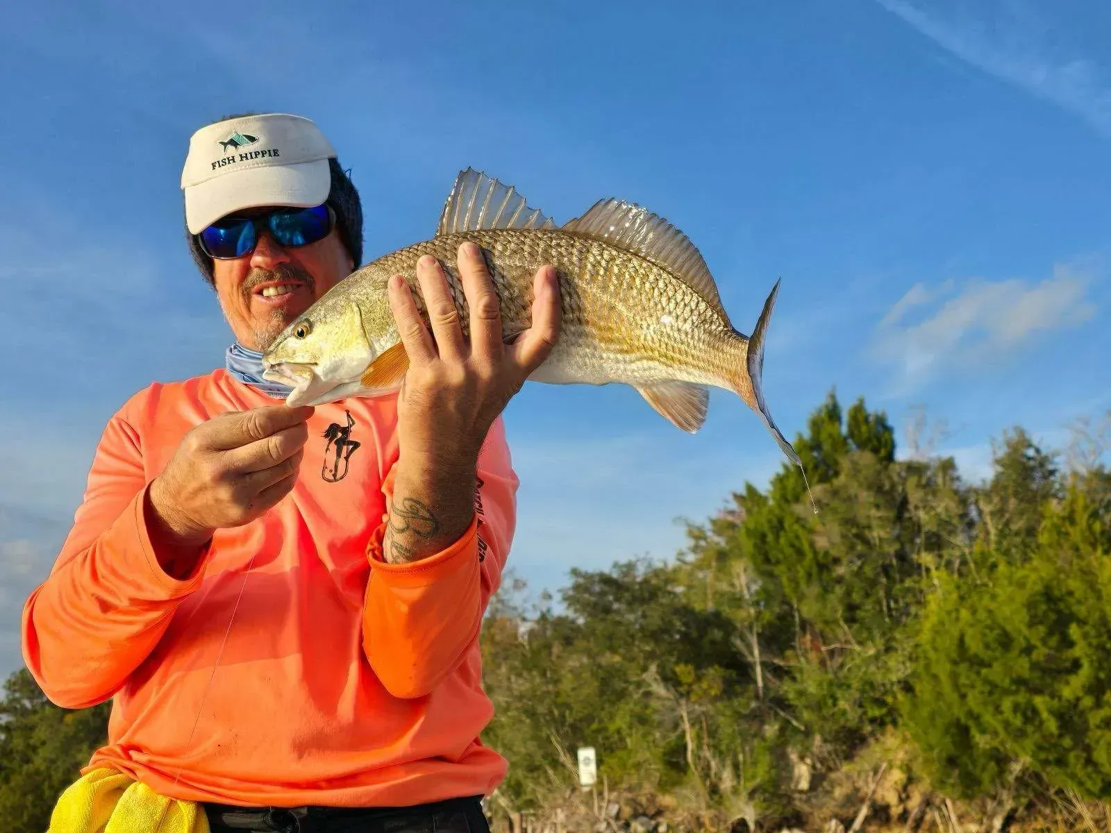 A man in an orange shirt is holding a large fish in his hands.
