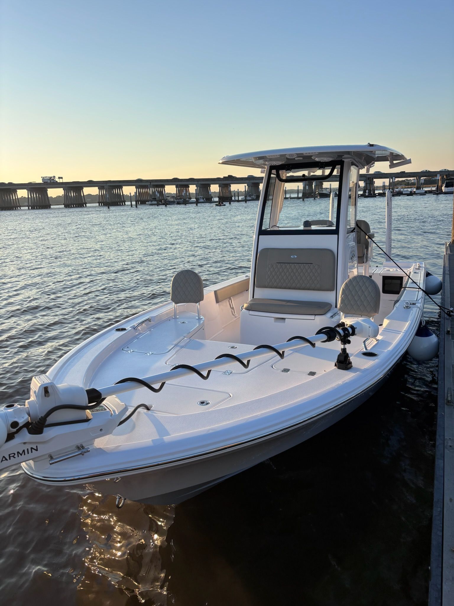 White fishing boat docked on water, bridge in background.