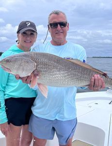A man and a woman are standing on a boat holding a large fish.