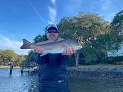 A man is holding a large fish in his hands in front of a body of water.