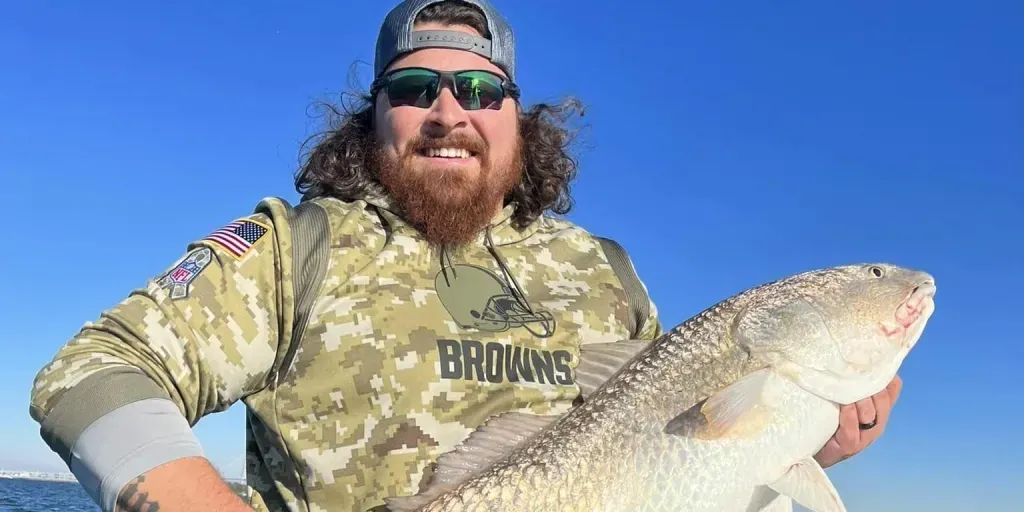A man in a camouflage shirt is holding a large fish.