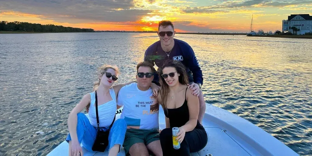 A group of people are sitting on a boat in the water at sunset.