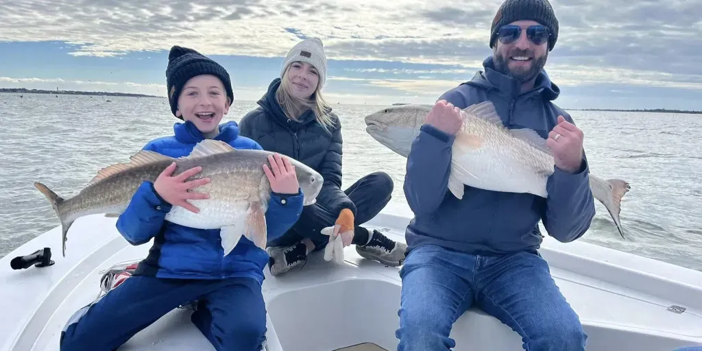 A man , woman and child are sitting on a boat holding fish.