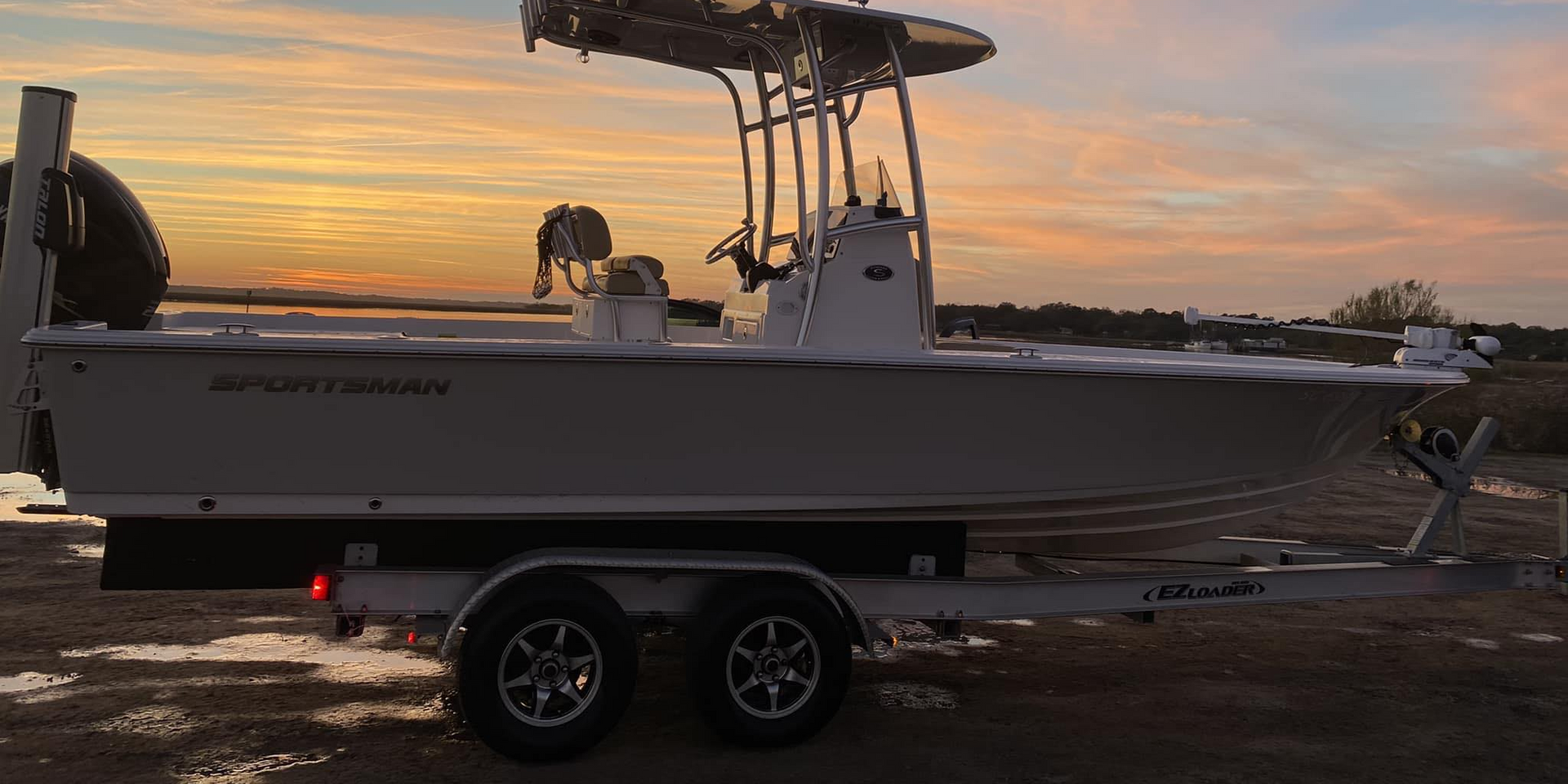 A boat is parked on a trailer in a field at sunset.
