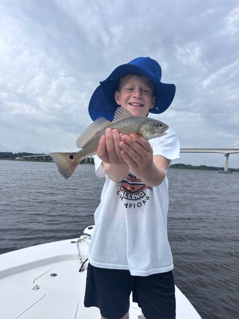 A young boy wearing a blue hat is holding a fish in his hands