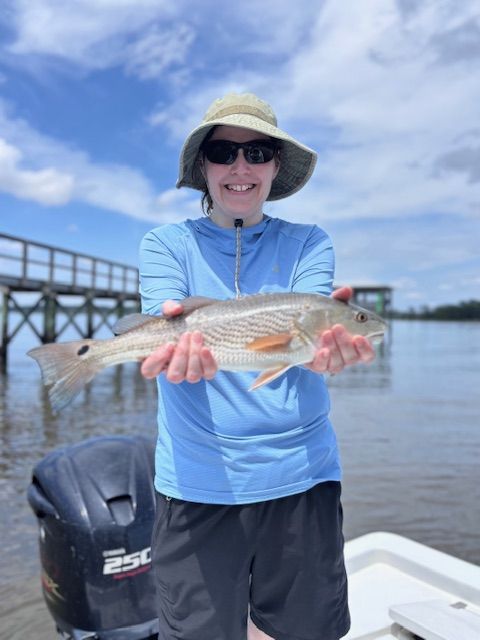 A woman holding a fish in front of a boat with a yamaha engine
