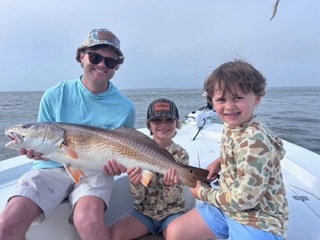 A man and two children on a boat holding a large fish