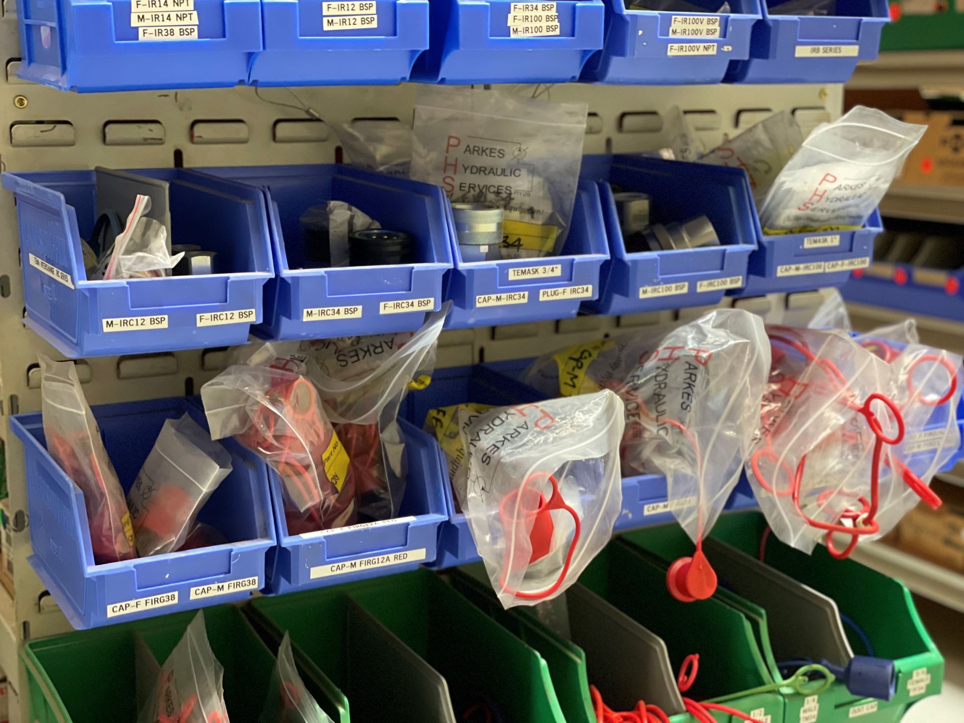 A shelf filled with blue bins and green bins filled with red bags.
