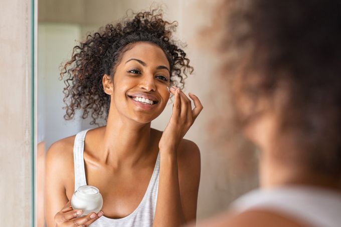 a woman applying cream to her face in front of a mirror