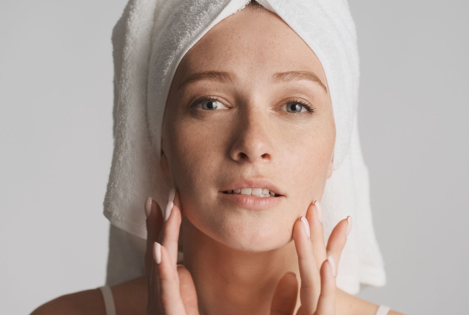 a woman with a towel wrapped around her head touches her face