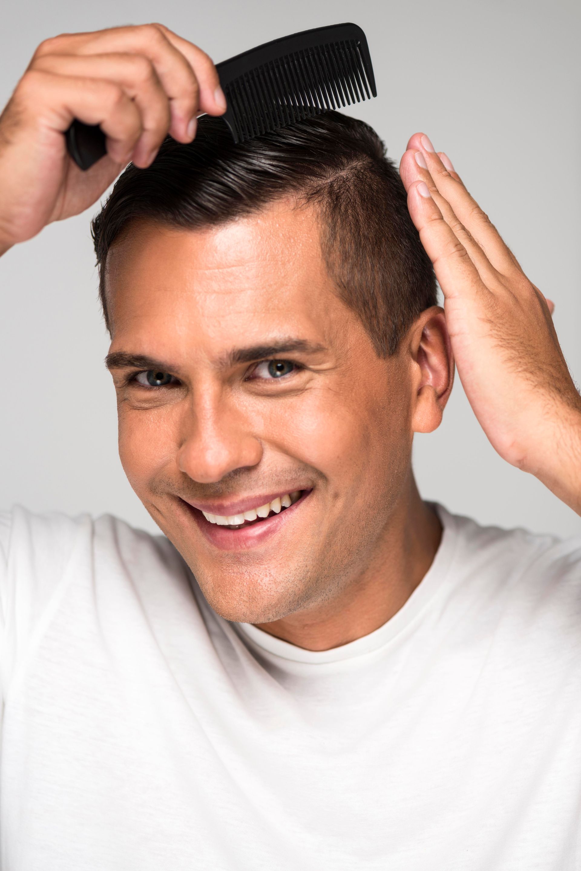 a man in a white shirt is smiling while combs his hair