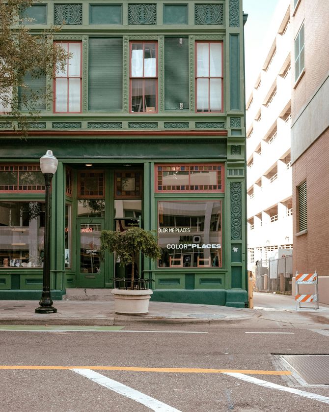 A green building with a lot of windows is on a city street.