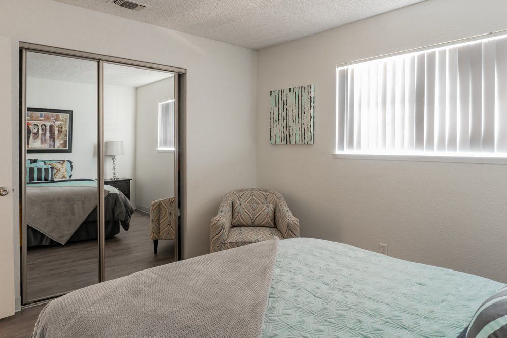 A bedroom with a bed , chair , and mirrored sliding glass doors.